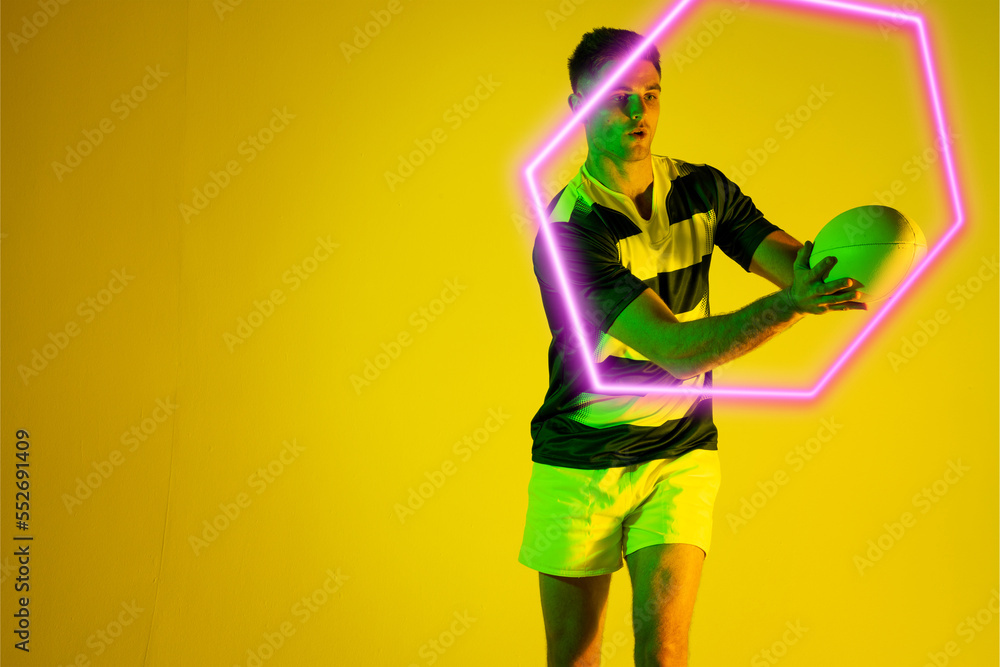 Caucasian male rugby player catching ball by illuminated hexagon over yellow background