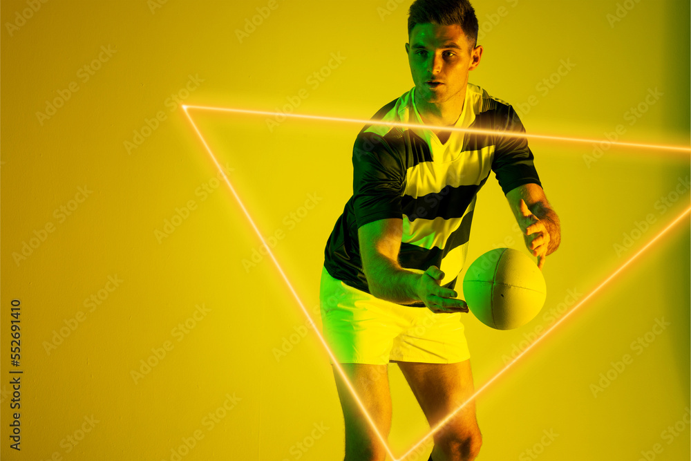 Caucasian male rugby player catching ball in front of illuminated triangle over yellow background