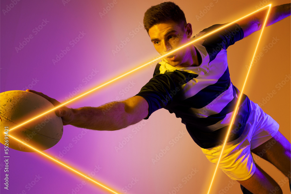 Caucasian male rugby player holding ball and jumping by illuminated triangle on graident background