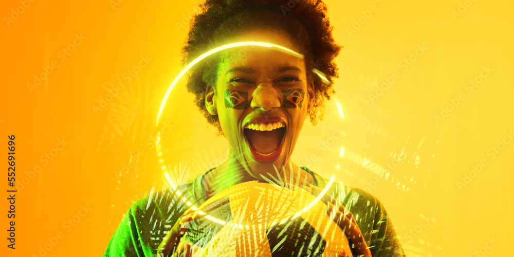 African american female fan with ball and brazilian face paint screaming by plants and circle