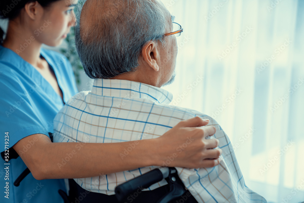 Rear view of a caregiver and her contented senior patient gazing out through the window. Elderly ill