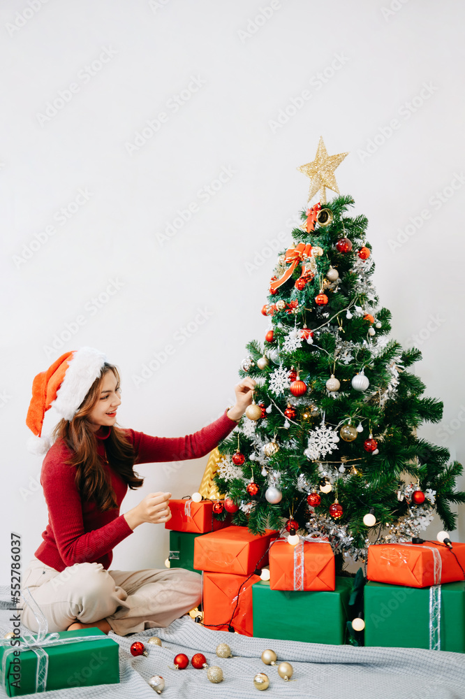  Female hand decorating christmas tree with toys. Sunlight floods the room.