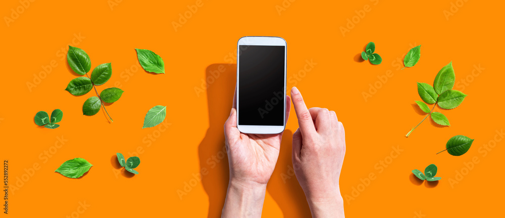 Person using a smartphone with green leaves - flat lay