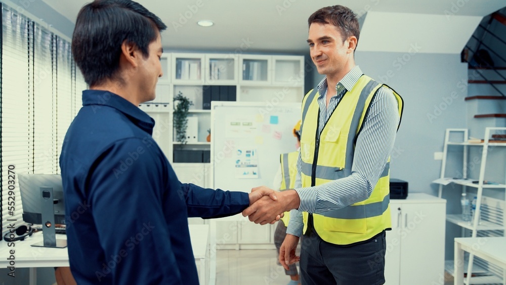 An engineer with a protective vest handshake with an investor in his office. Following a successful 