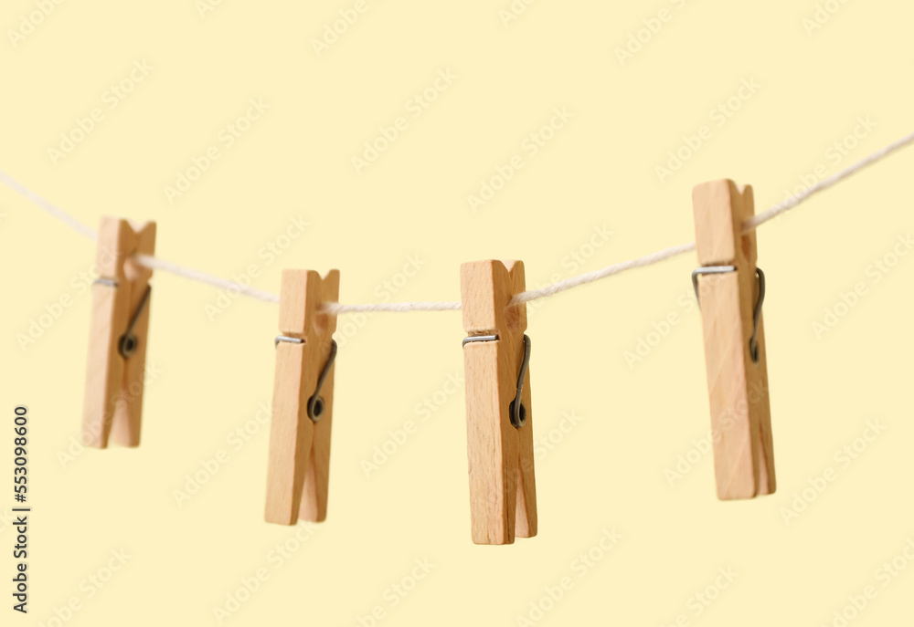 Wooden clothespins hanging on rope against color background