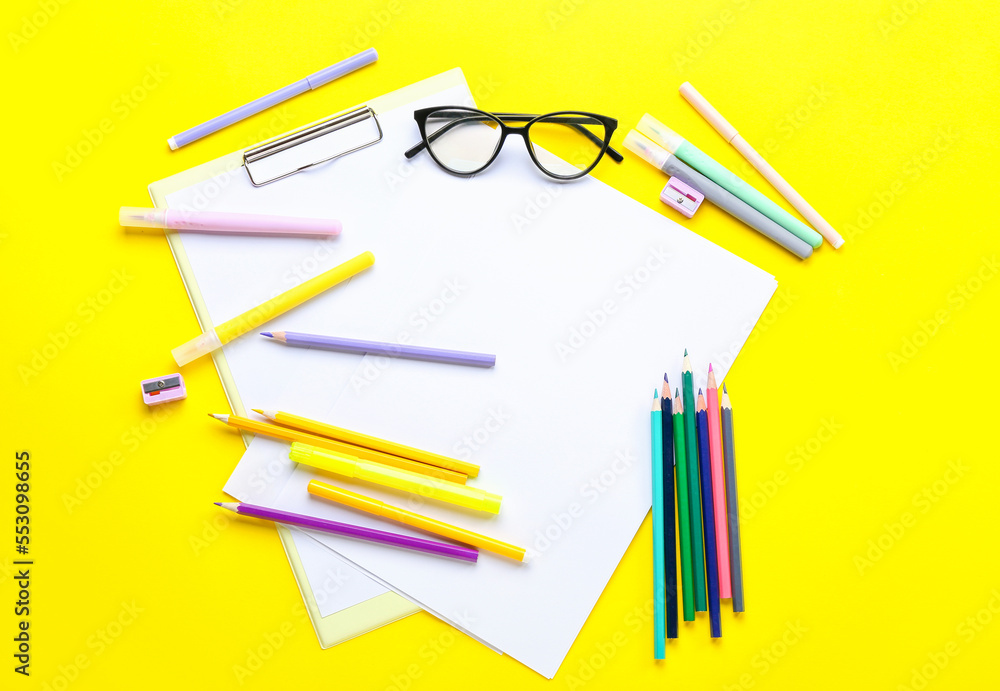 Clipboard with blank paper sheets, felt-tip pens, pencils, sharpeners and eyeglasses on yellow backg