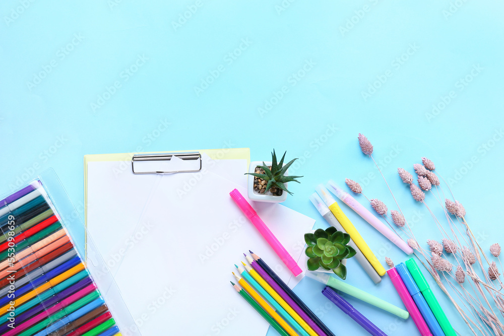 Blank paper sheet with felt-tip pens, pencils, pots and dried flowers on blue background