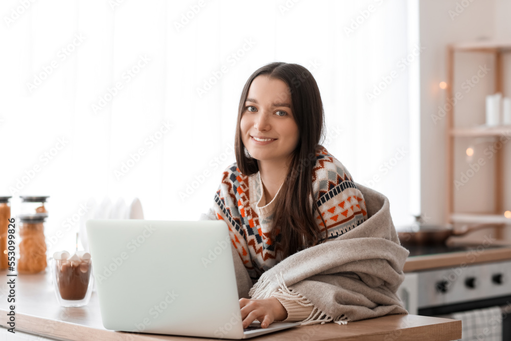 Young woman in warm plaid using laptop in kitchen