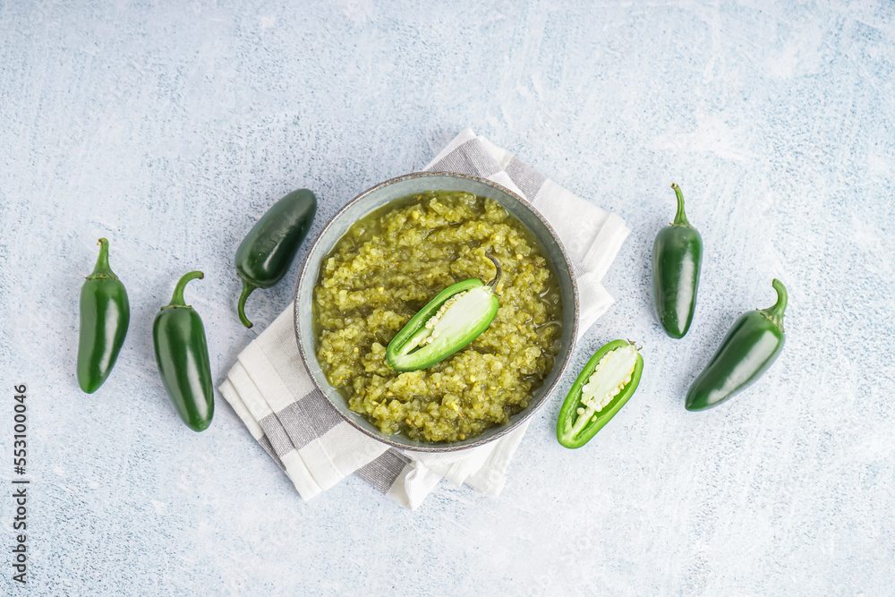 Bowl of tasty green salsa sauce and fresh jalapeno peppers on light background