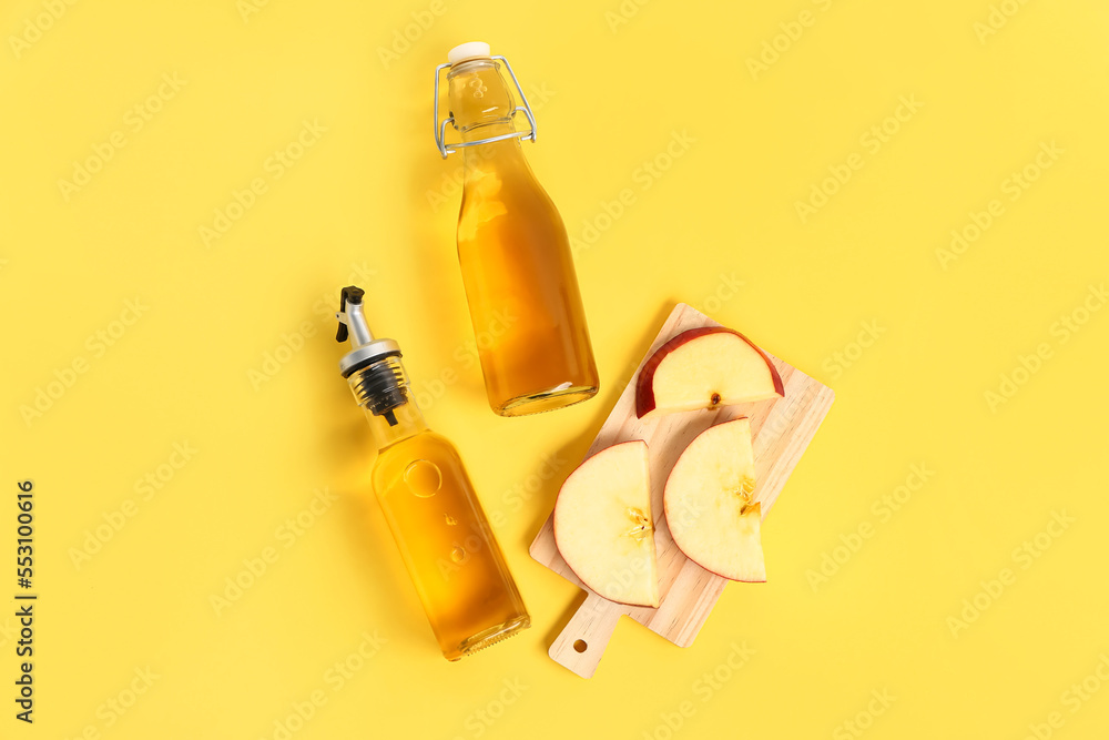 Bottles of apple cider vinegar and board with fruits on yellow background