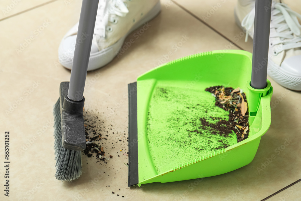 Woman sweeping tile floor with dustpan and broom, closeup