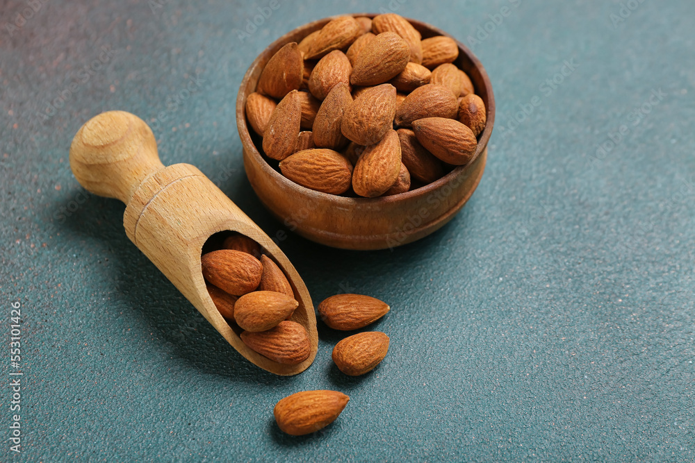 Bowl of almonds with wooden scoop on green background