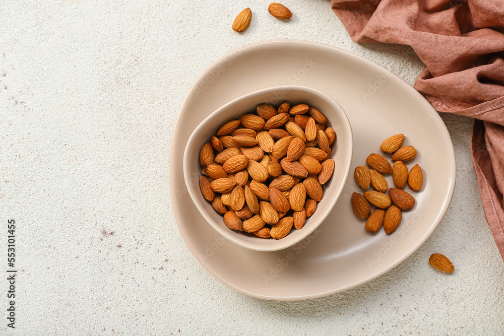 Plate with bowl of almonds on white background