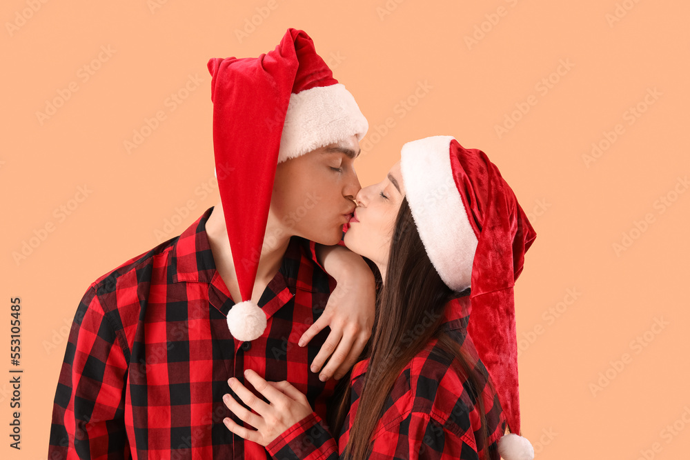 Young couple in Santa hats kissing on beige background, closeup