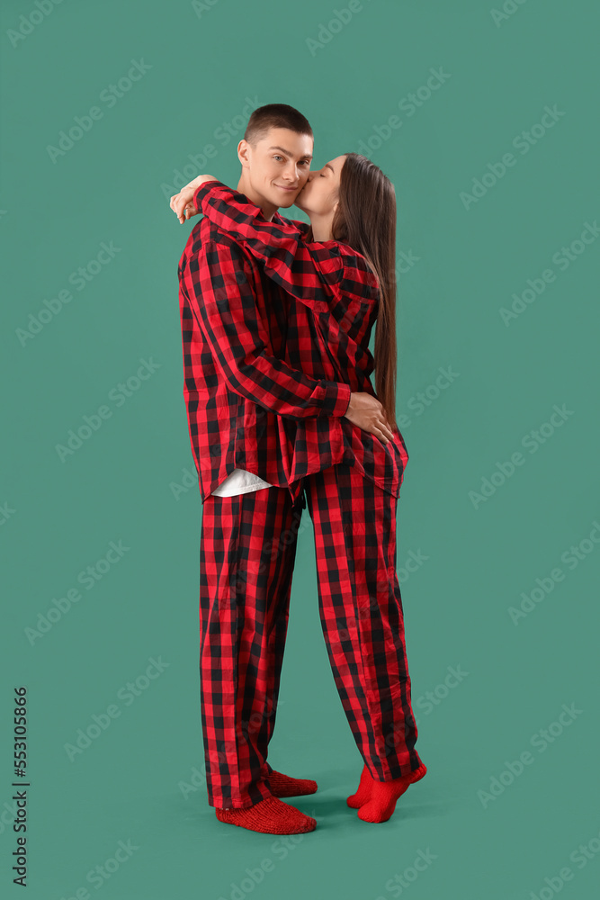 Young couple in checkered pajamas hugging on green background