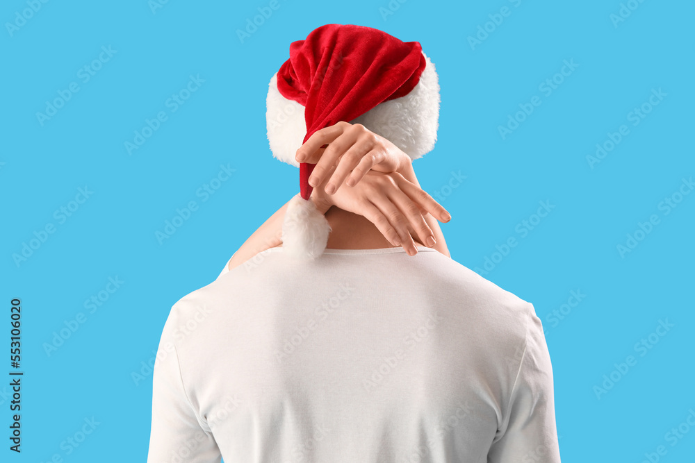 Young couple in Santa hat hugging on blue background, back view