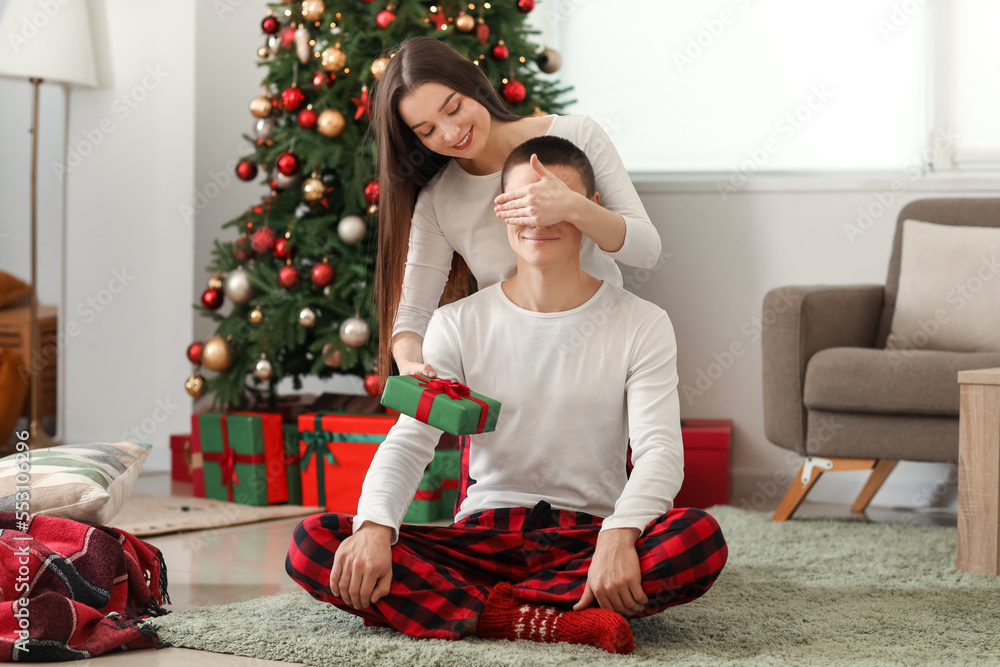 Young woman surprising her boyfriend with Christmas gift at home