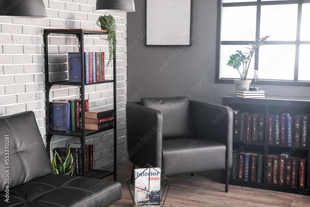 Shelf unit with books, sofa and armchair near grey brick wall in library interior