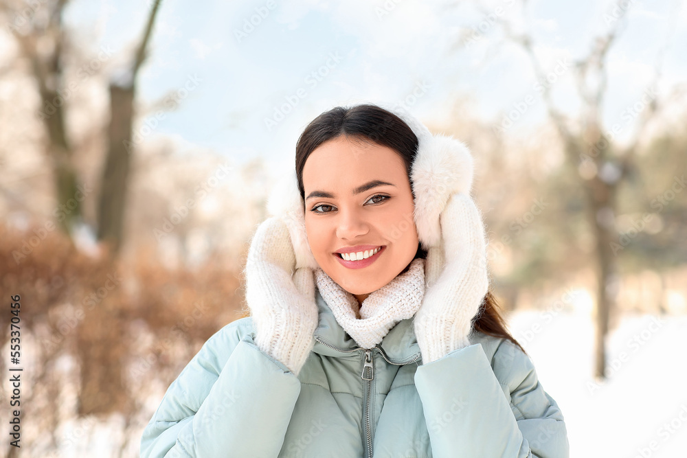 Beautiful smiling woman in warm clothes and earmuffs on cold winter day