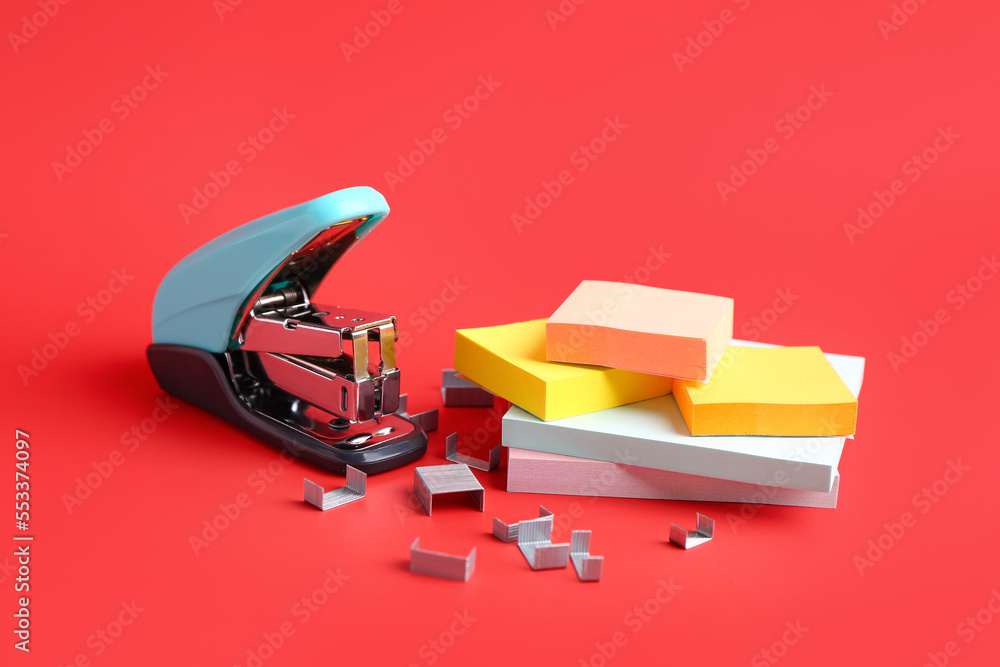 Stapler, staples and sticky notes on red background