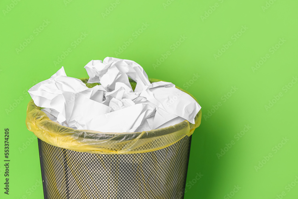 Office bin with crumpled paper on green background, closeup