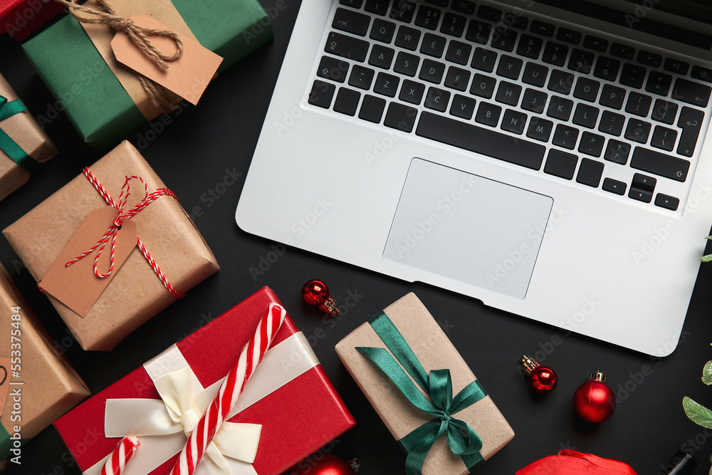 Laptop with Christmas decor and gifts on black background