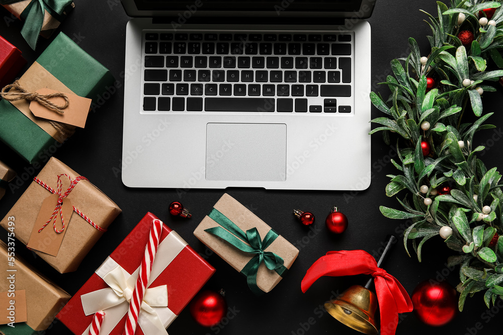 Laptop with Christmas decor and gifts on black background