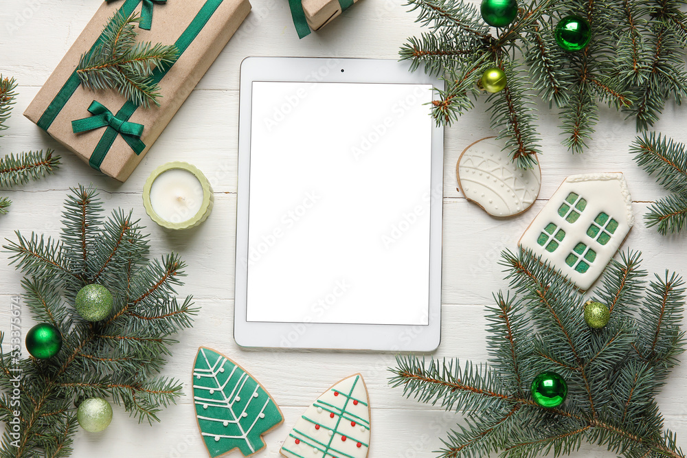 Blank tablet computer with Christmas decor, cookies and gifts on white wooden background