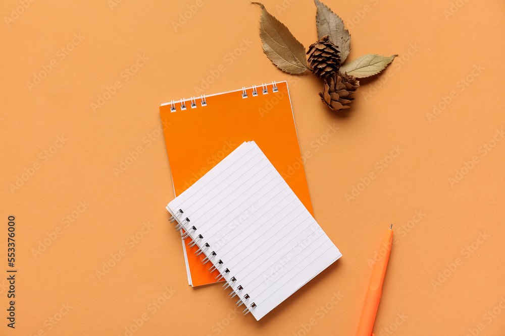 Notebooks, autumn leaves, cones and pen on color background