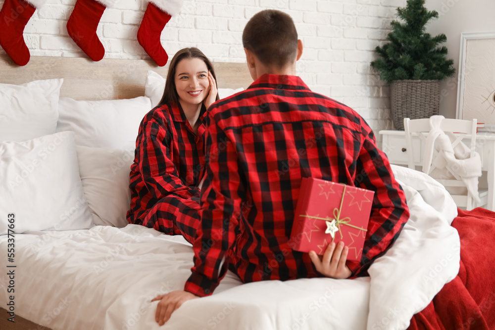 Young man surprising his wife with Christmas gift in bedroom