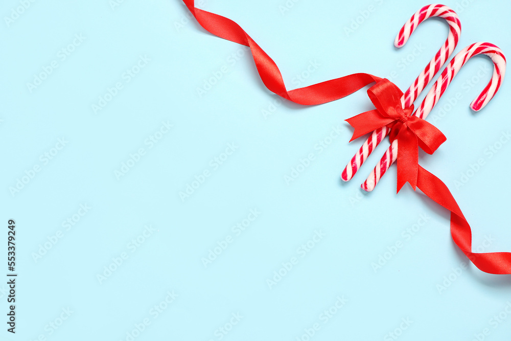 Sweet candy canes tied with red ribbon on color background