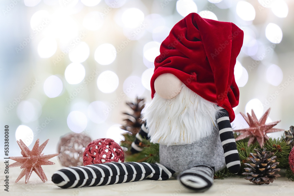 Christmas gnome, fir branches and decorations on table against blurred lights