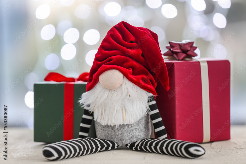 Christmas gnome and gift boxes on table against blurred lights