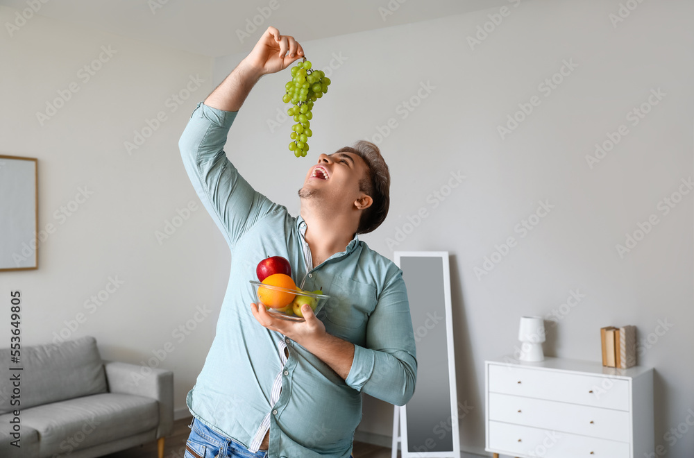 Young overweight man with bowl of fruits at home