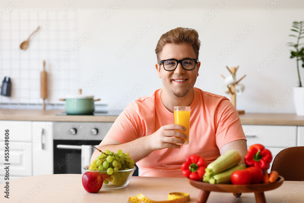 Young overweight man with glass of juice in kitchen