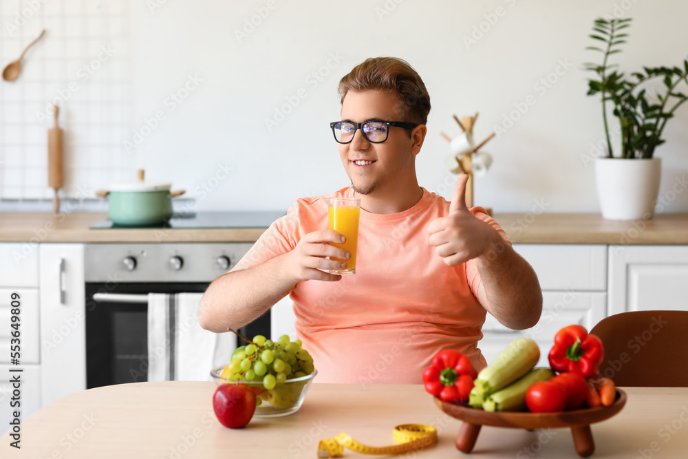 厨房里一杯果汁的超重年轻男子竖起大拇指