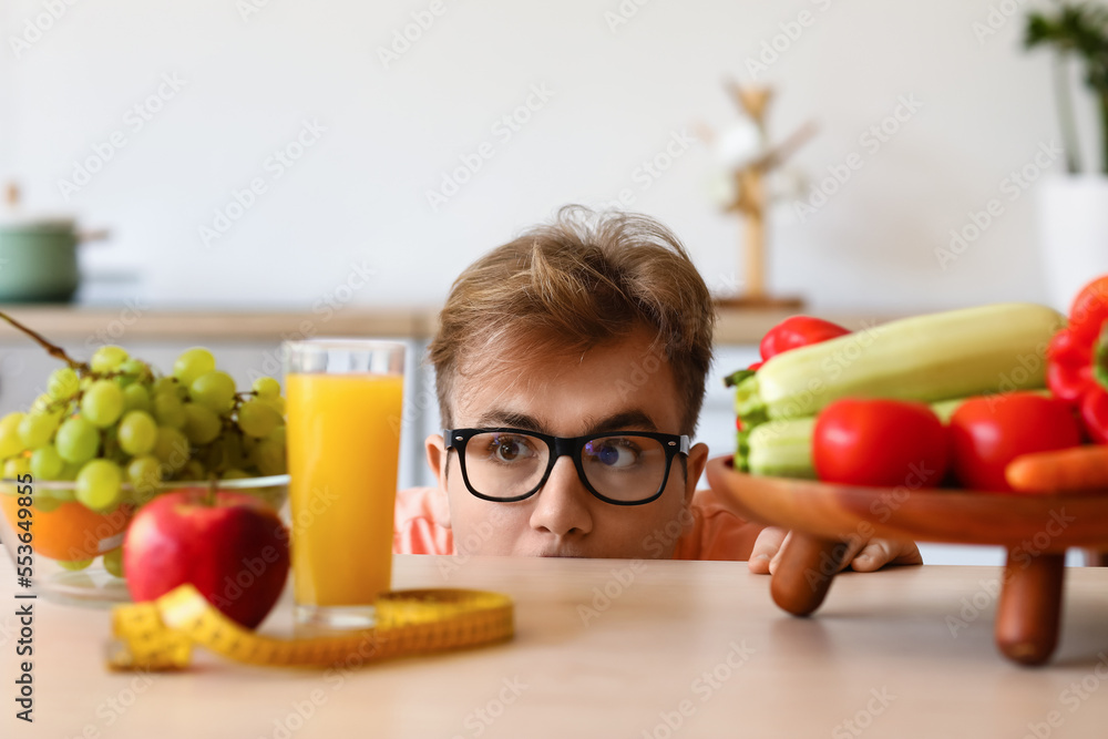 Young overweight man with healthy food, glass of juice and measuring tape at table in kitchen, close