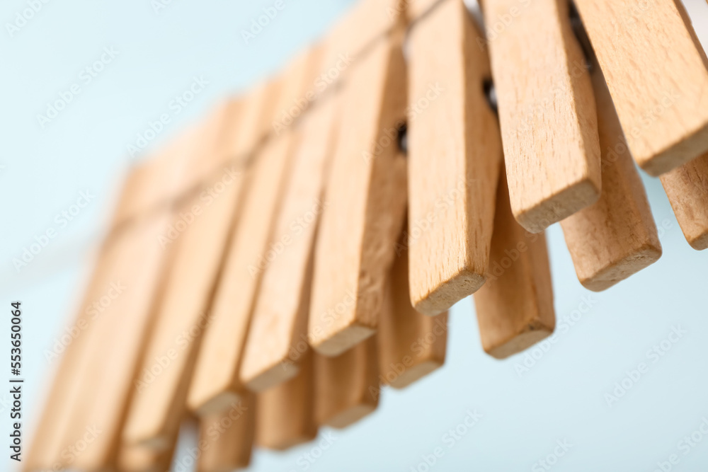 Wooden clothespins hanging on rope against blue background, closeup