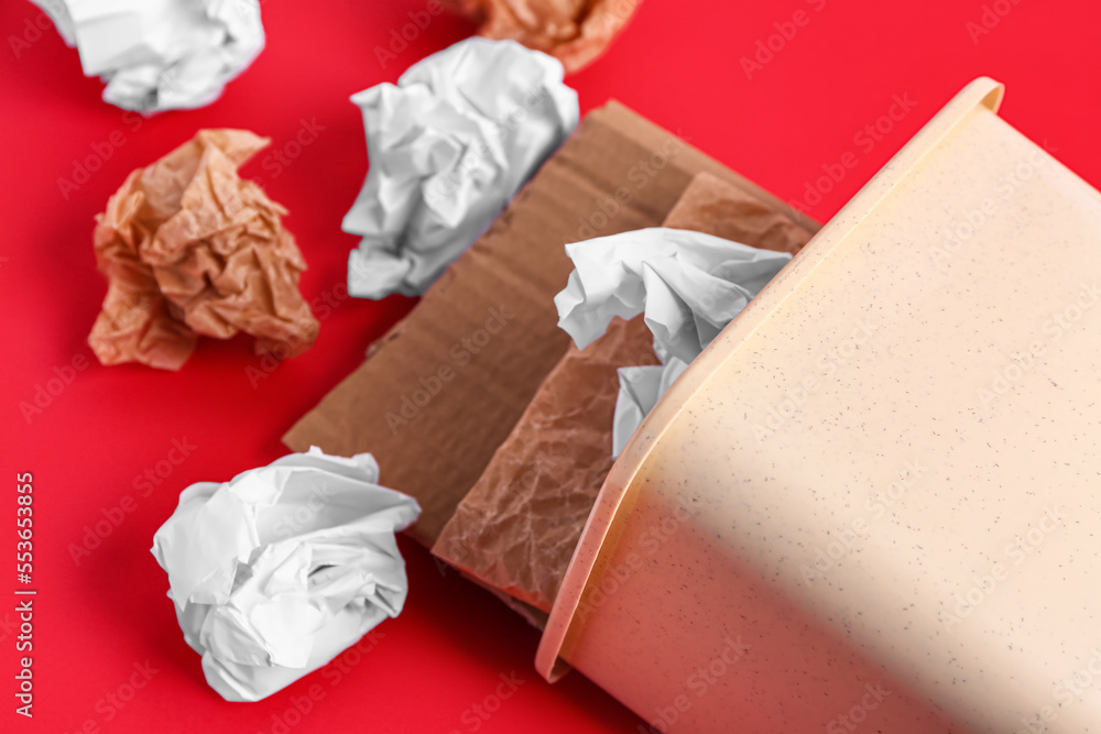 Overturned rubbish bin with garbage on red background, closeup