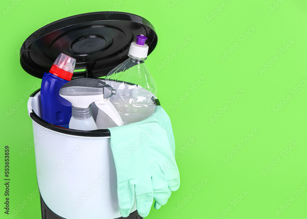 Rubbish bin with cleaning supplies on green background