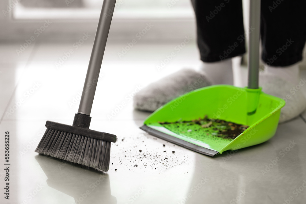 Woman sweeping tile floor with broom and dustpan, closeup