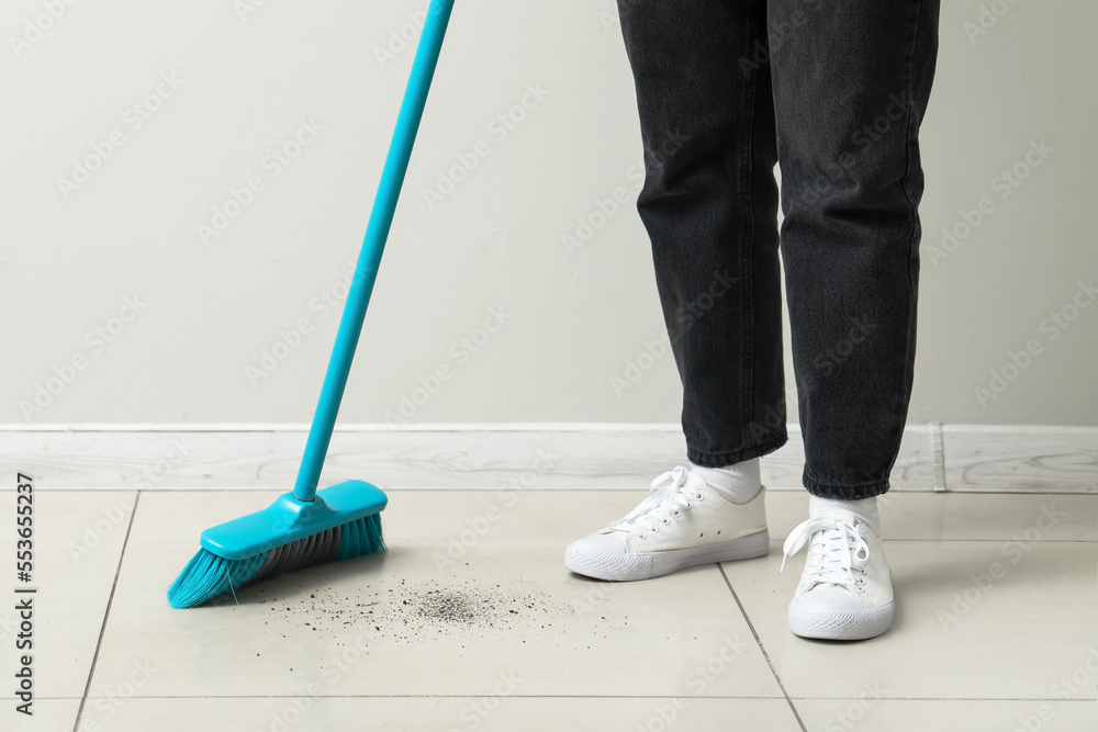 Woman sweeping light tile floor with broom