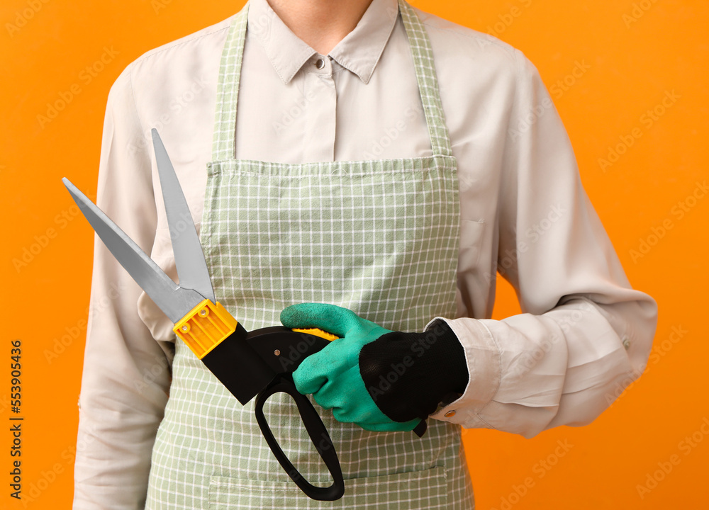 Female gardener with pruner on orange background, closeup