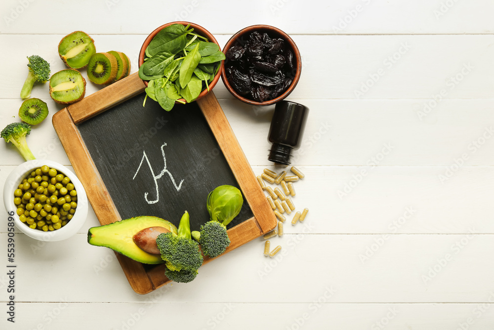 Chalkboard with letter K, healthy products and bottle of pills on white wooden background