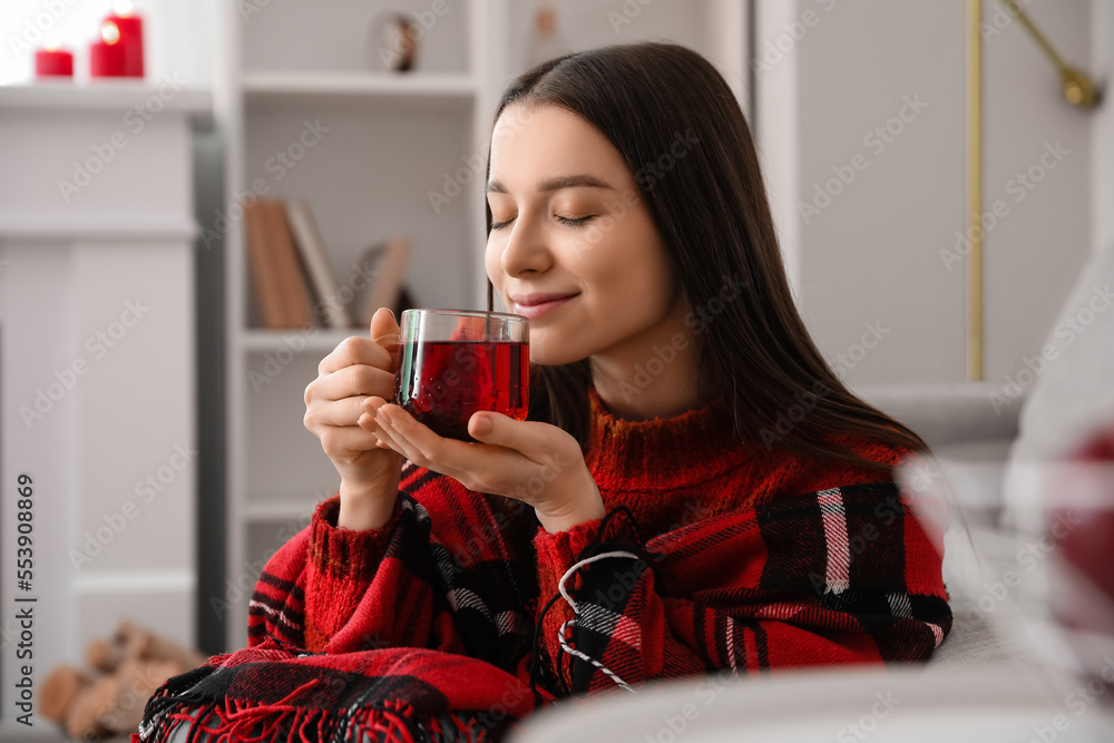 Young woman in warm plaid with glass cup of tea at home