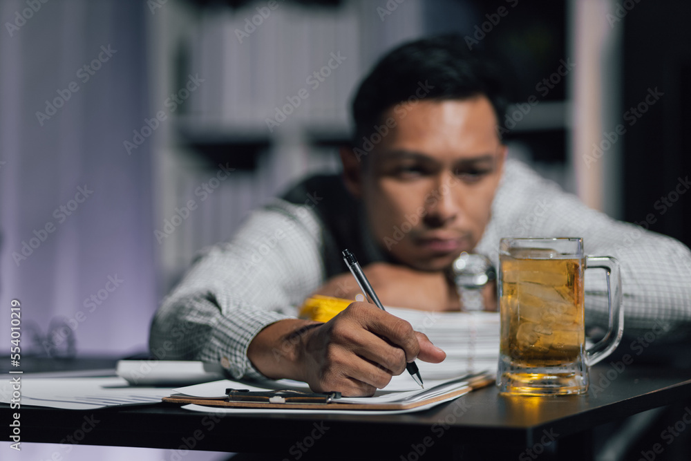 Businessman in the night office drinking beer while working overtime.