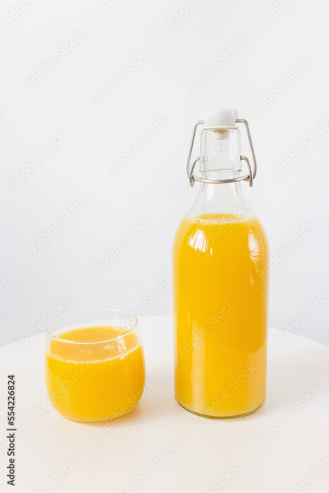 Fresh squeezed orange juice in bottle and glass on table on white