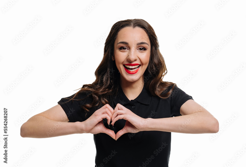 Portrait of a smiling young woman showing heart gesture with two hands and looking at camera isolate