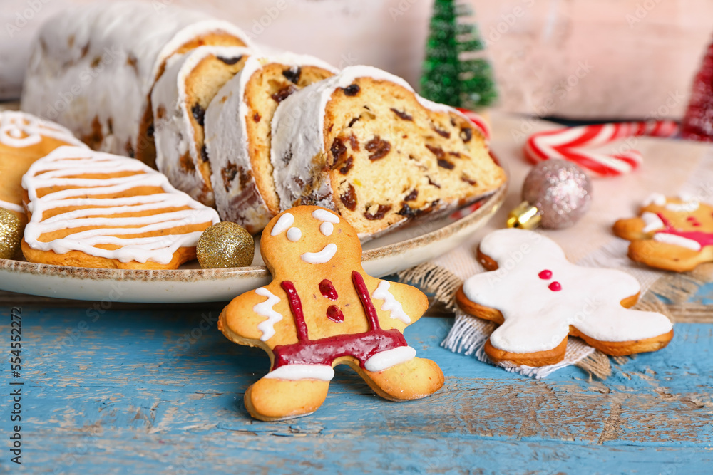 Plate with tasty Christmas stollen, cookies and decorations on color wooden table, closeup