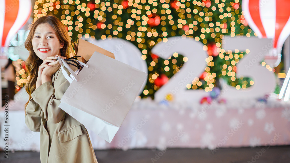 Beautiful asian girl hold shopping bags on Christmas tree bokeh light background at night, happy new